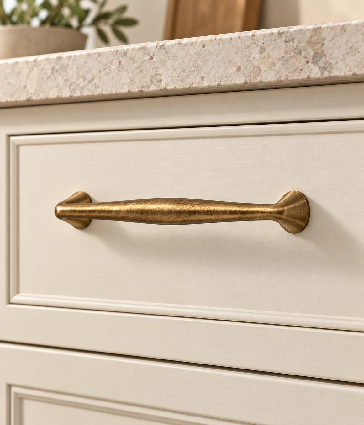 Antique brass tapered cabinet pull installed on a cream drawer