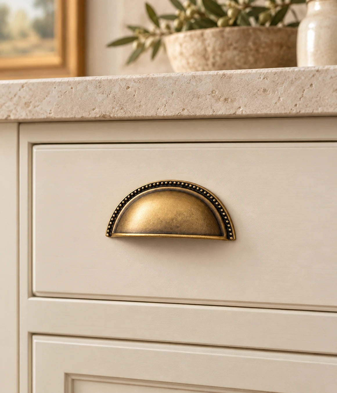 Antique brass beaded cup pull installed on a cream cabinet drawer