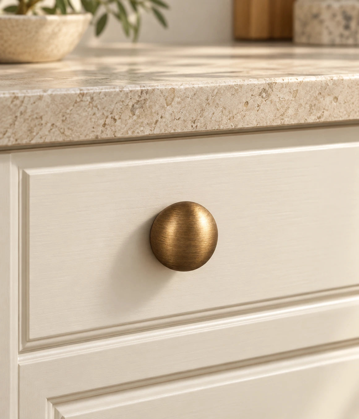 Smooth antique brass round cabinet knob installed on a cream drawer