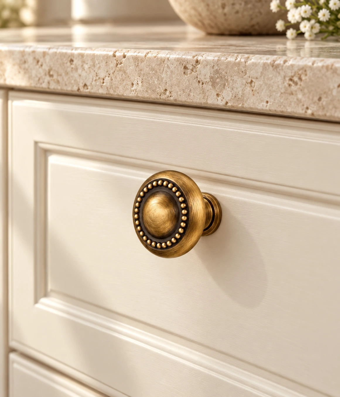Antique brass beaded cabinet knob installed on a cream drawer