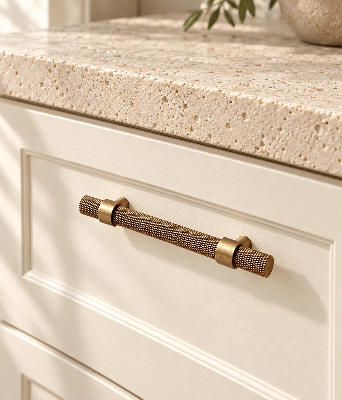 Antique brass knurled cabinet pull installed on a cream drawer