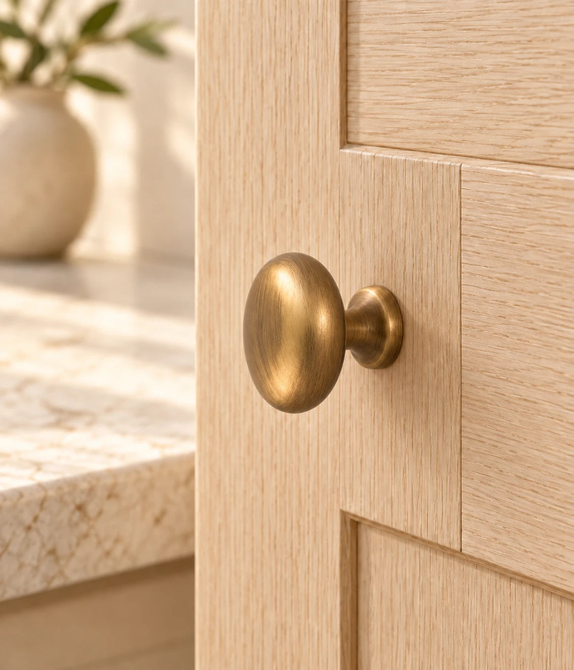 Antique brass mushroom knob mounted on a light oak cabinet door