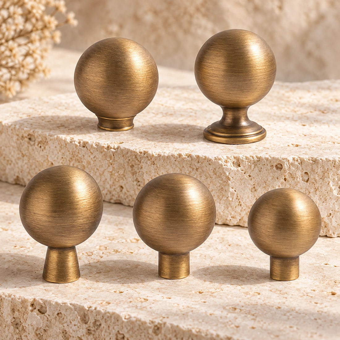 Five antique brass ball cabinet knobs with different stem profiles on limestone