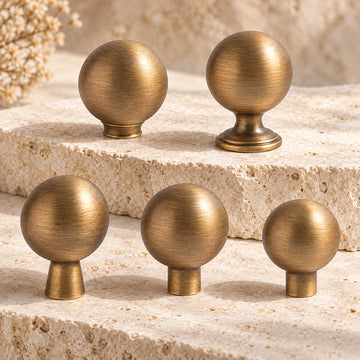 Five antique brass ball cabinet knobs with different stem profiles on limestone
