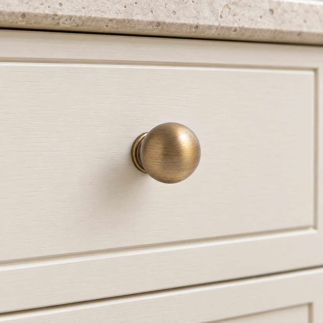Five antique brass ball cabinet knobs with different stem profiles on limestone