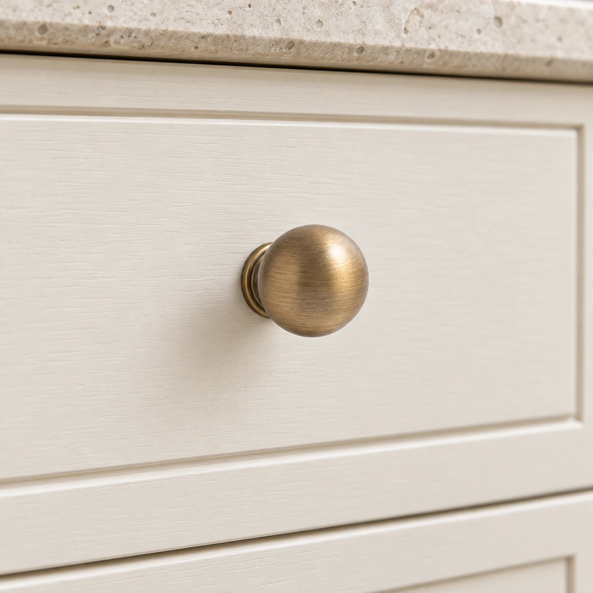 Antique brass ball knob with pedestal base installed on an ivory cabinet drawer