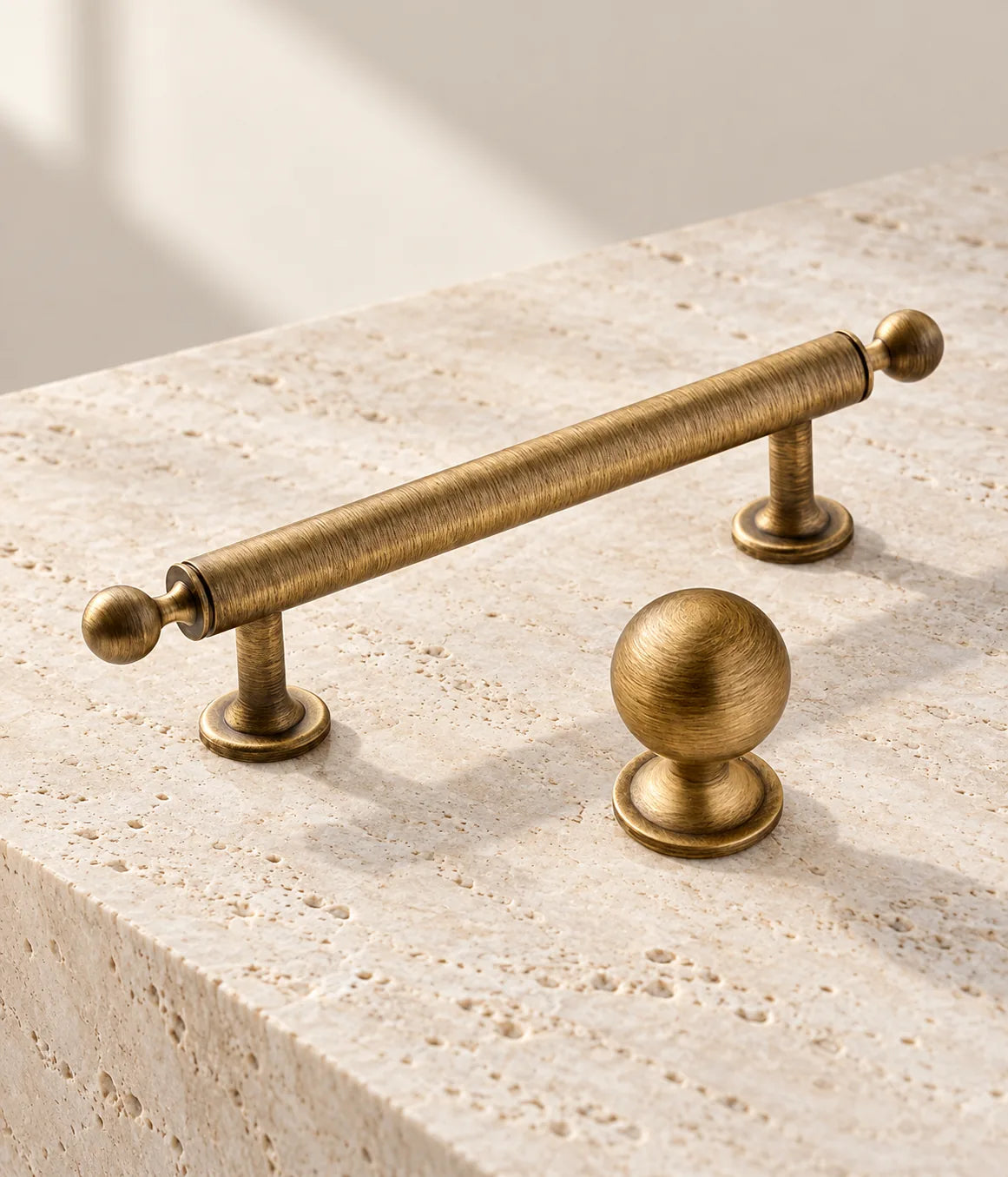 Close view of a solid brass ball-finial cabinet pull and round knob in antique brushed brass