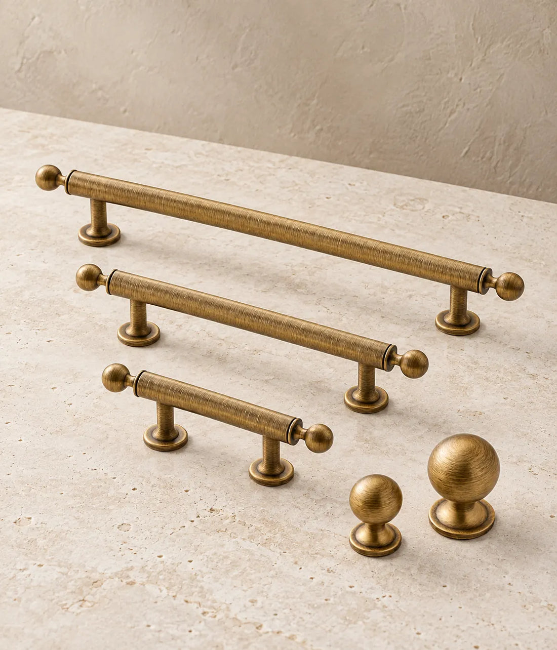 Antique brushed brass ball-finial cabinet pulls and round knobs arranged on pale limestone