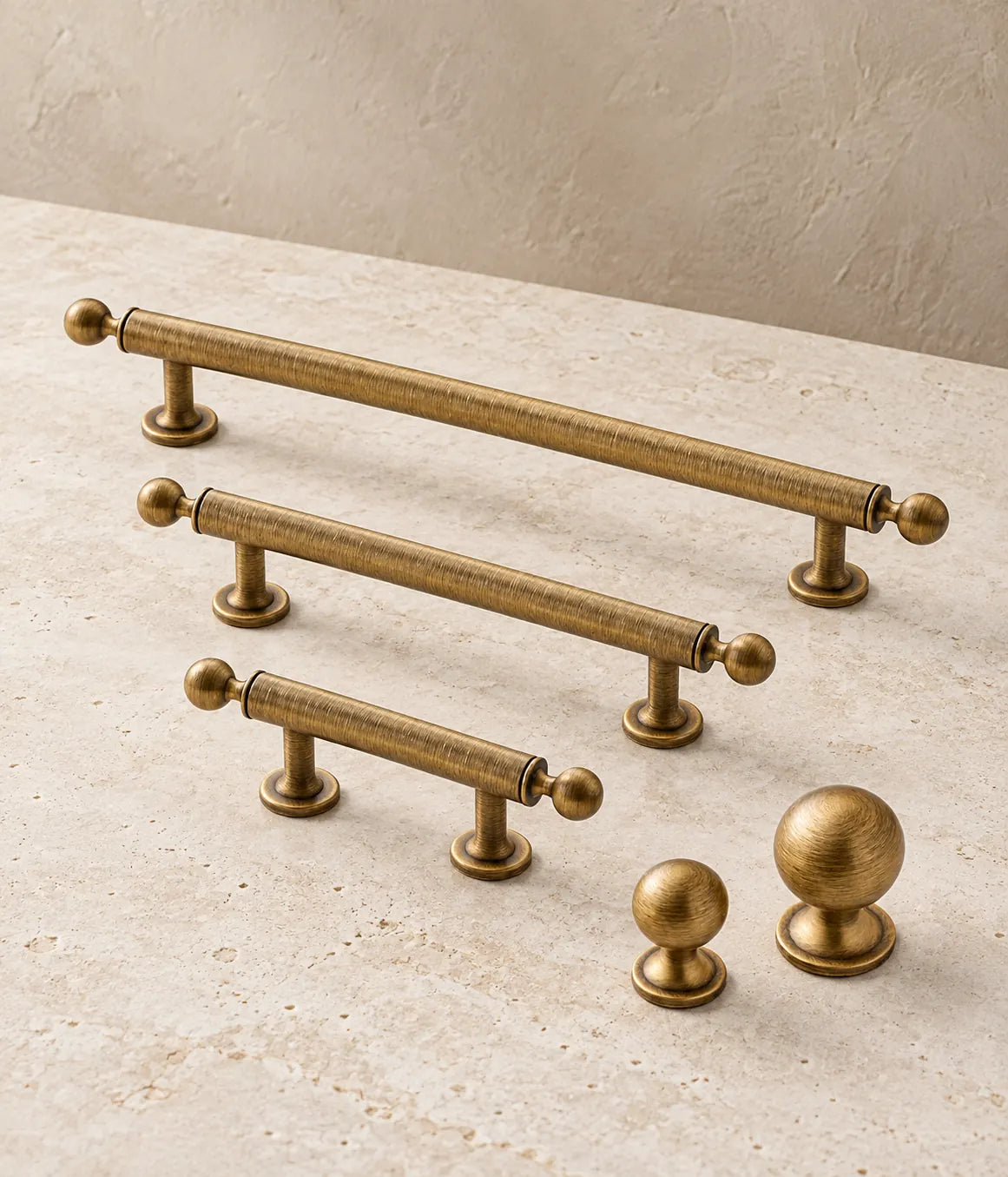 Antique brushed brass ball-finial cabinet pulls and round knobs arranged on pale limestone