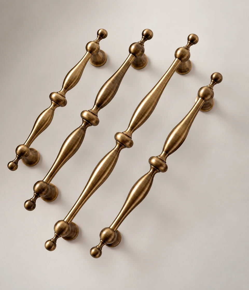 Four antique brass baluster cabinet pulls arranged on a neutral surface