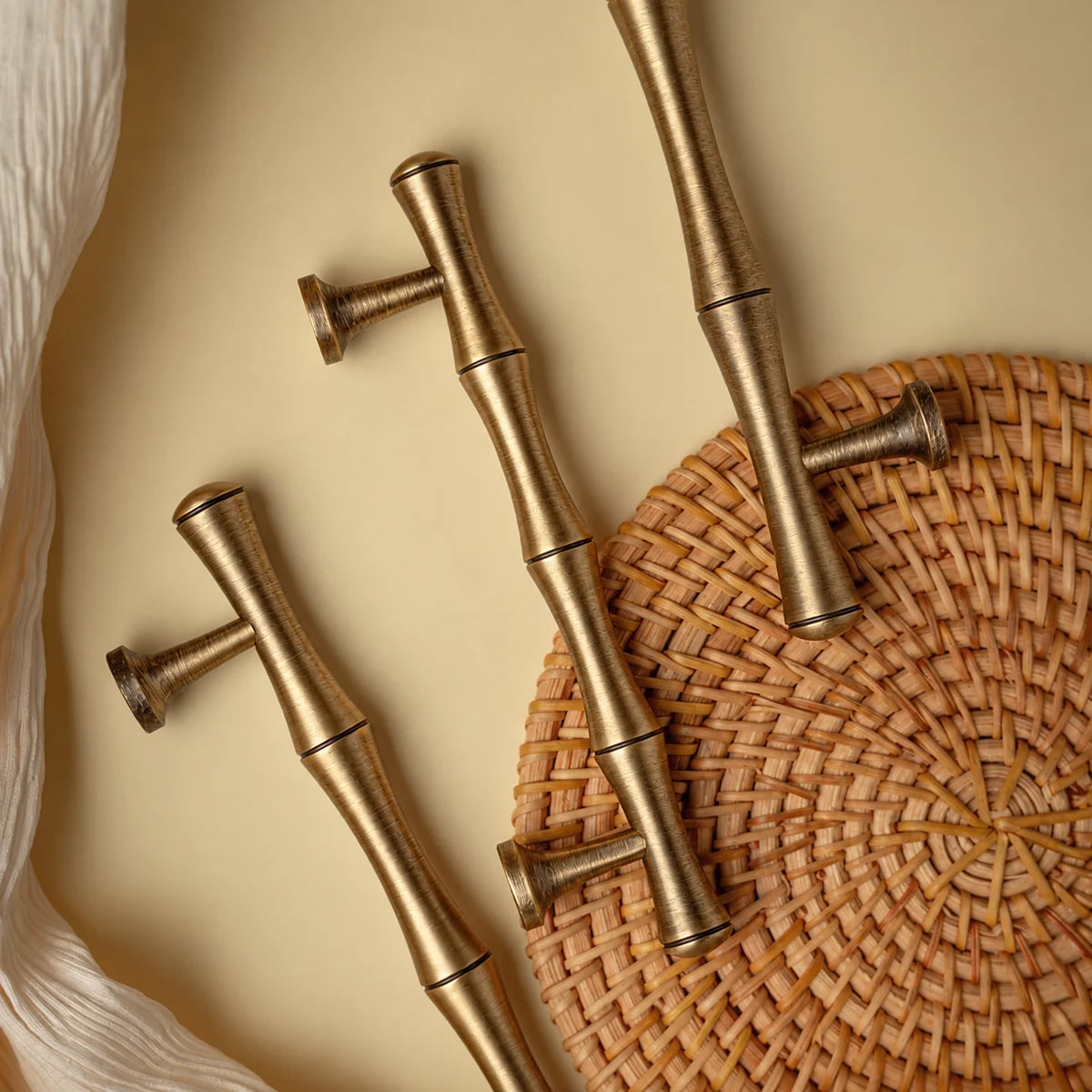 Close-up of bamboo-shaped antique brass pulls beside woven rattan and cream cloth