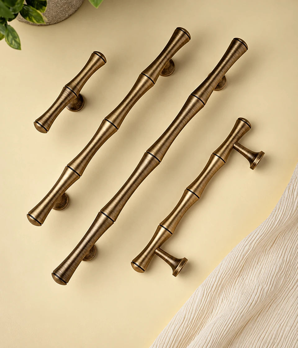Three antique brass bamboo cabinet pulls and matching T-knob on pale yellow surface