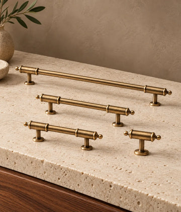 Antique brass barrel-collar cabinet pulls and matching ball-tip T-knob on pale limestone