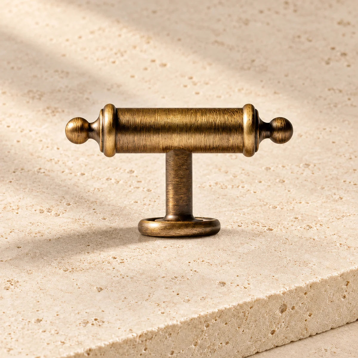 antique brass barrel collar t bar cabinet knob on pale limestone.