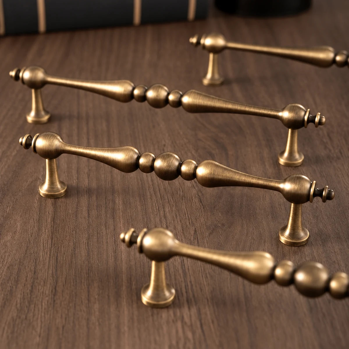 Four antique brass cabinet pulls with beaded centers arranged on a dark wood surface