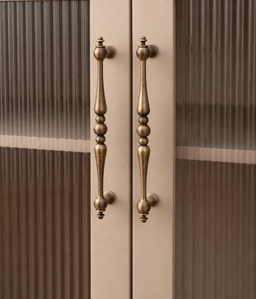 Antique brass beaded-center cabinet pulls installed vertically on cream doors with ribbed glass