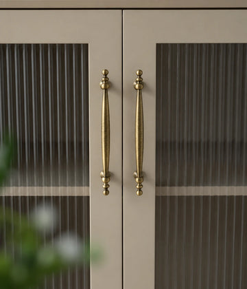 Antique brass beaded-end cabinet pulls installed vertically on cream ribbed-glass doors