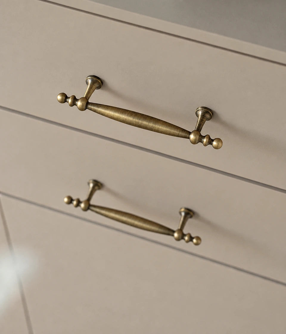 Antique brass spindle-grip handles mounted horizontally on cream drawers