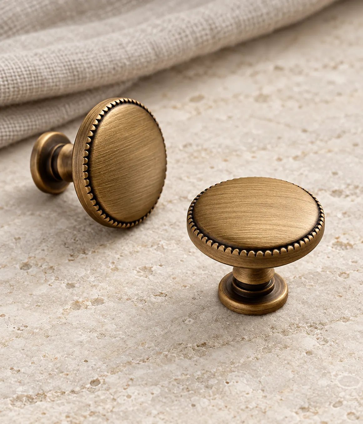 Antique brass beaded-rim disc cabinet knobs arranged on pale limestone