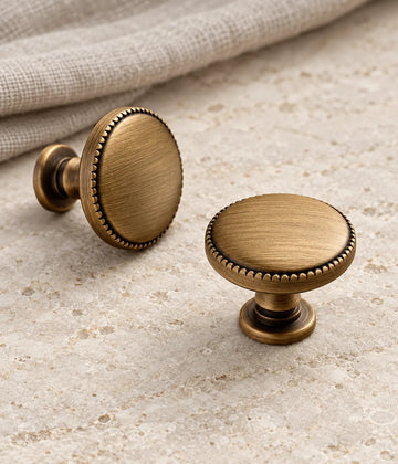 Antique brass beaded-rim disc cabinet knobs arranged on pale limestone