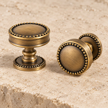 Antique brass beaded-rim cabinet knob with turned stem on pale limestone