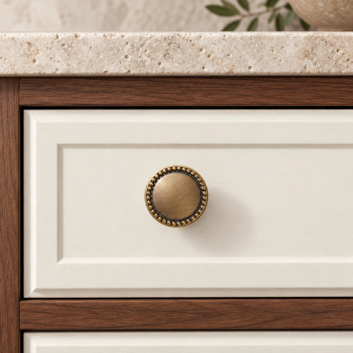 Antique brass beaded-rim knob mounted on an ivory cabinet drawer