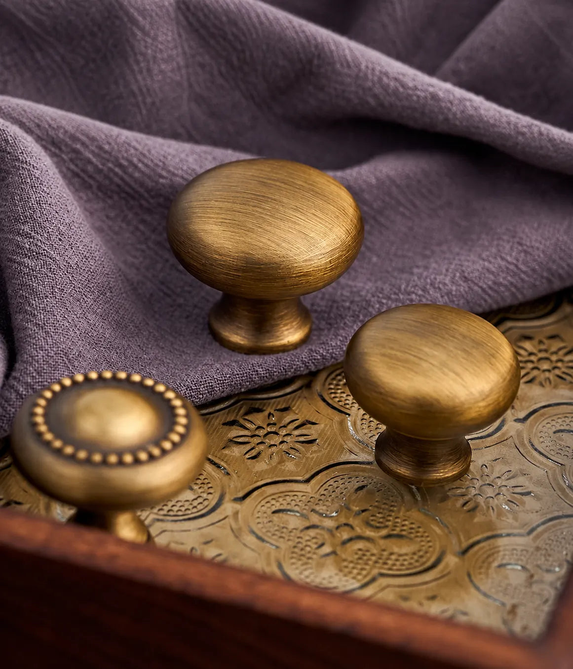 Beaded and smooth antique brass cabinet knobs on a decorative tray and fabric