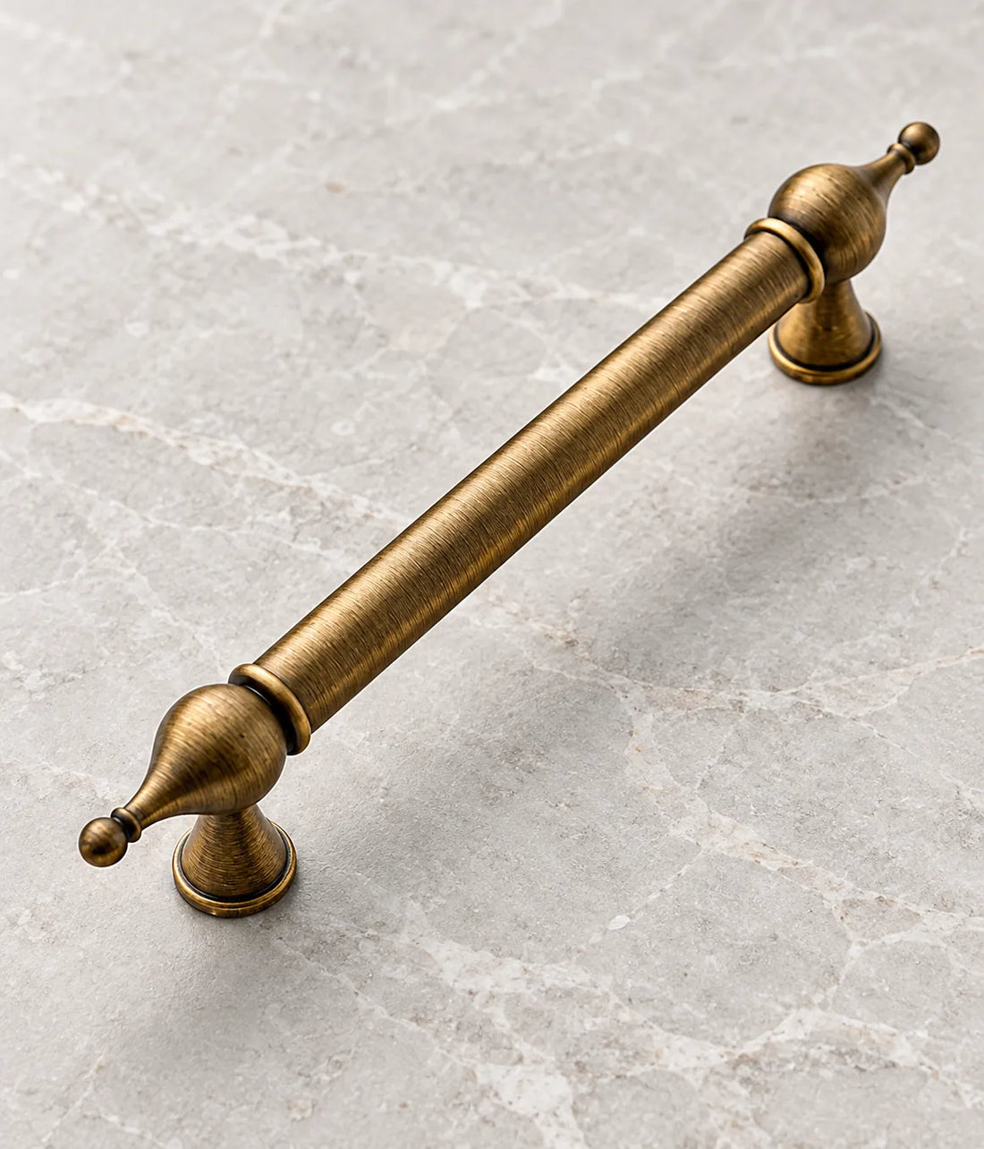 Antique brass bulb-finial cabinet pulls and matching T-knob arranged on pale limestone