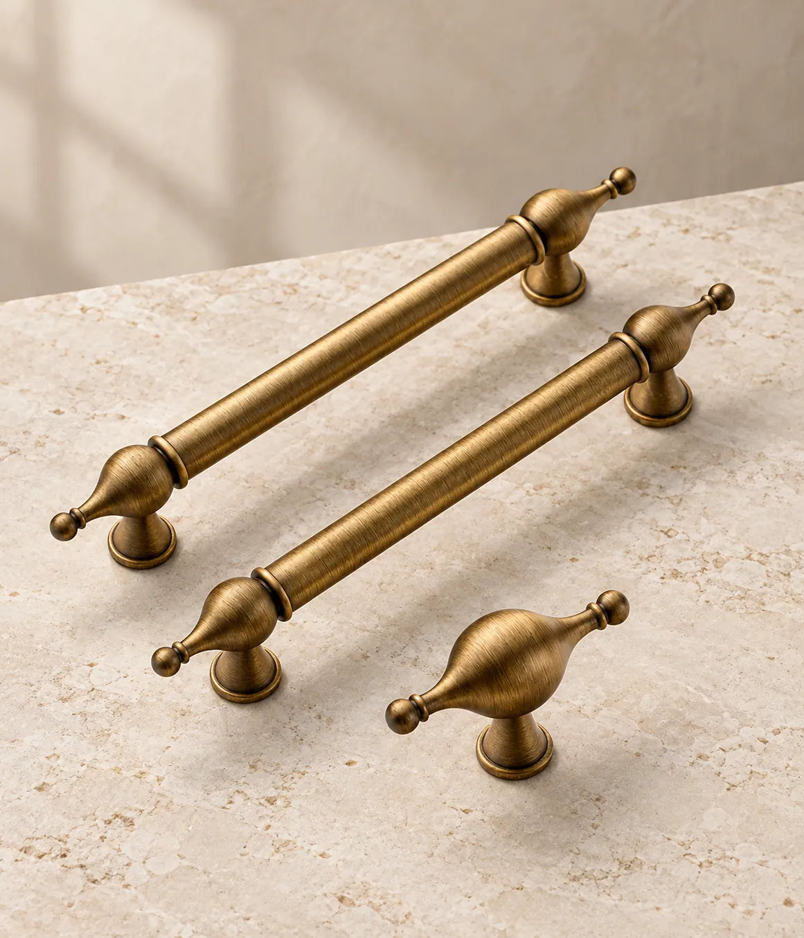 Antique brass bulb-finial cabinet pulls and matching T-knob arranged on pale limestone