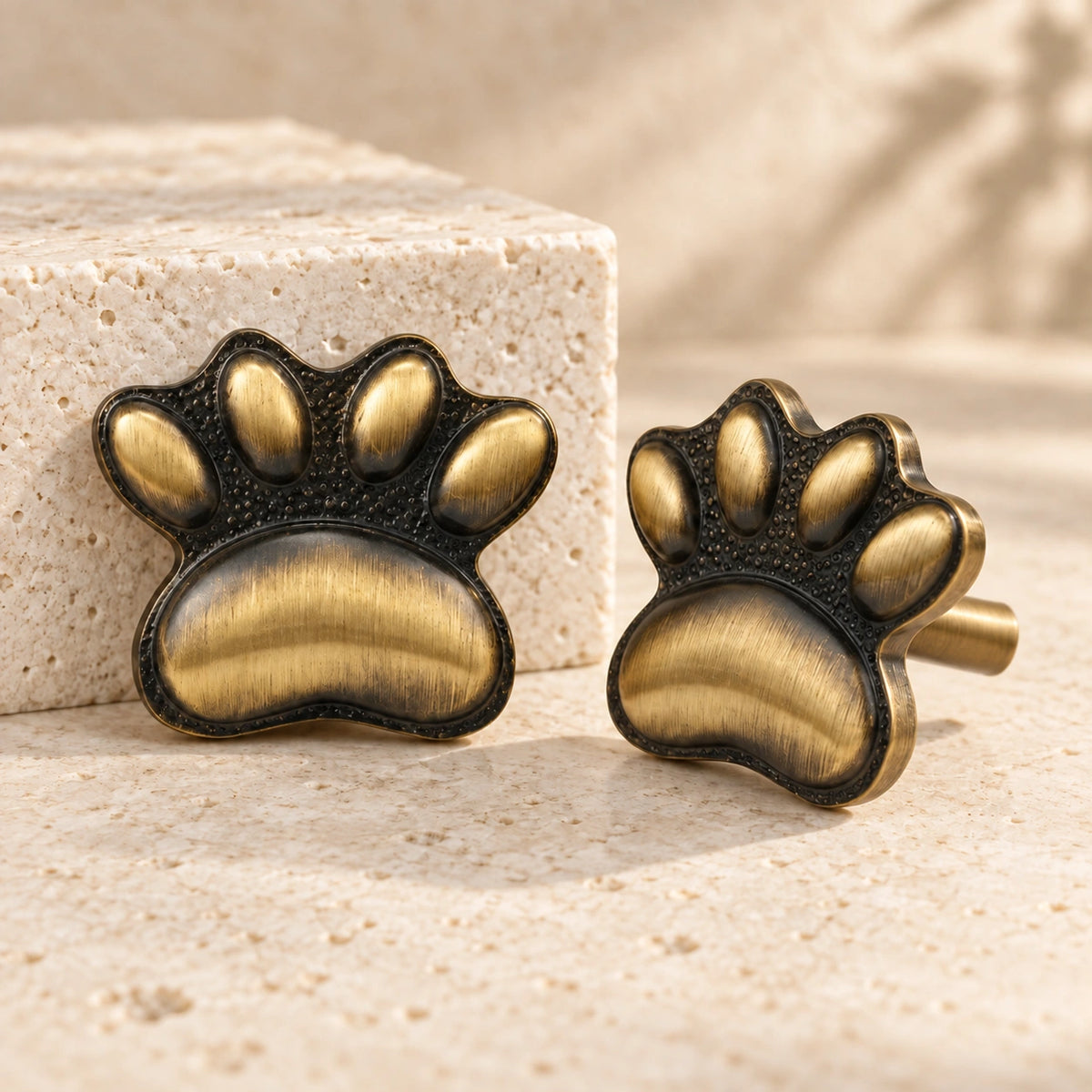 Antique brass cat paw cabinet knobs on limestone, showing the textured paw face and straight mounting stem