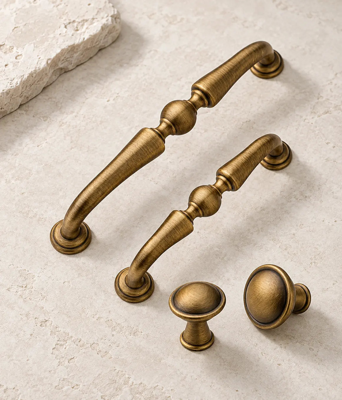 Antique brushed brass center-ball cabinet pulls and domed knobs arranged on pale limestone