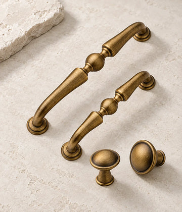 Antique brushed brass center-ball cabinet pulls and domed knobs arranged on pale limestone