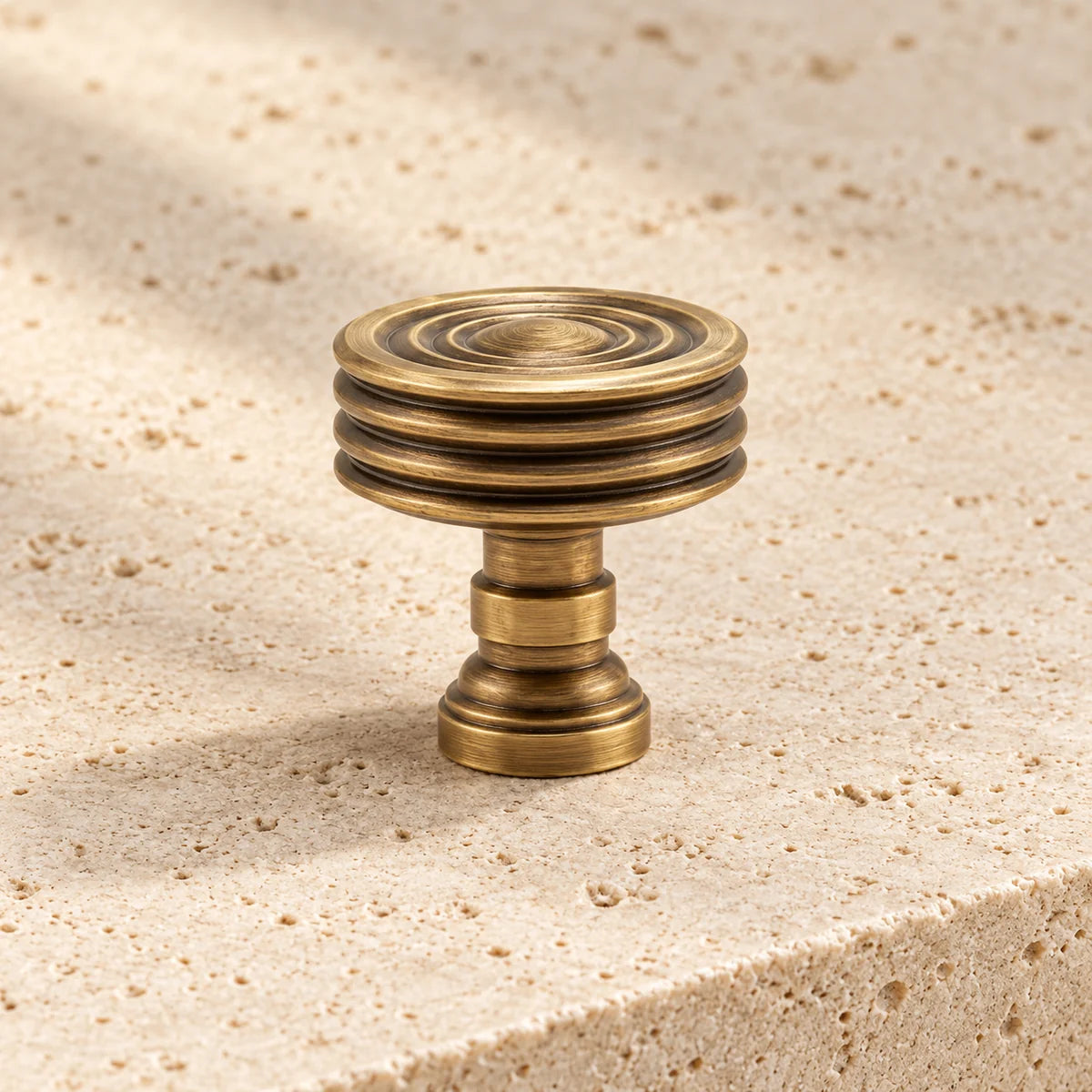 antique brass concentric ring cabinet knob on pale limestone.