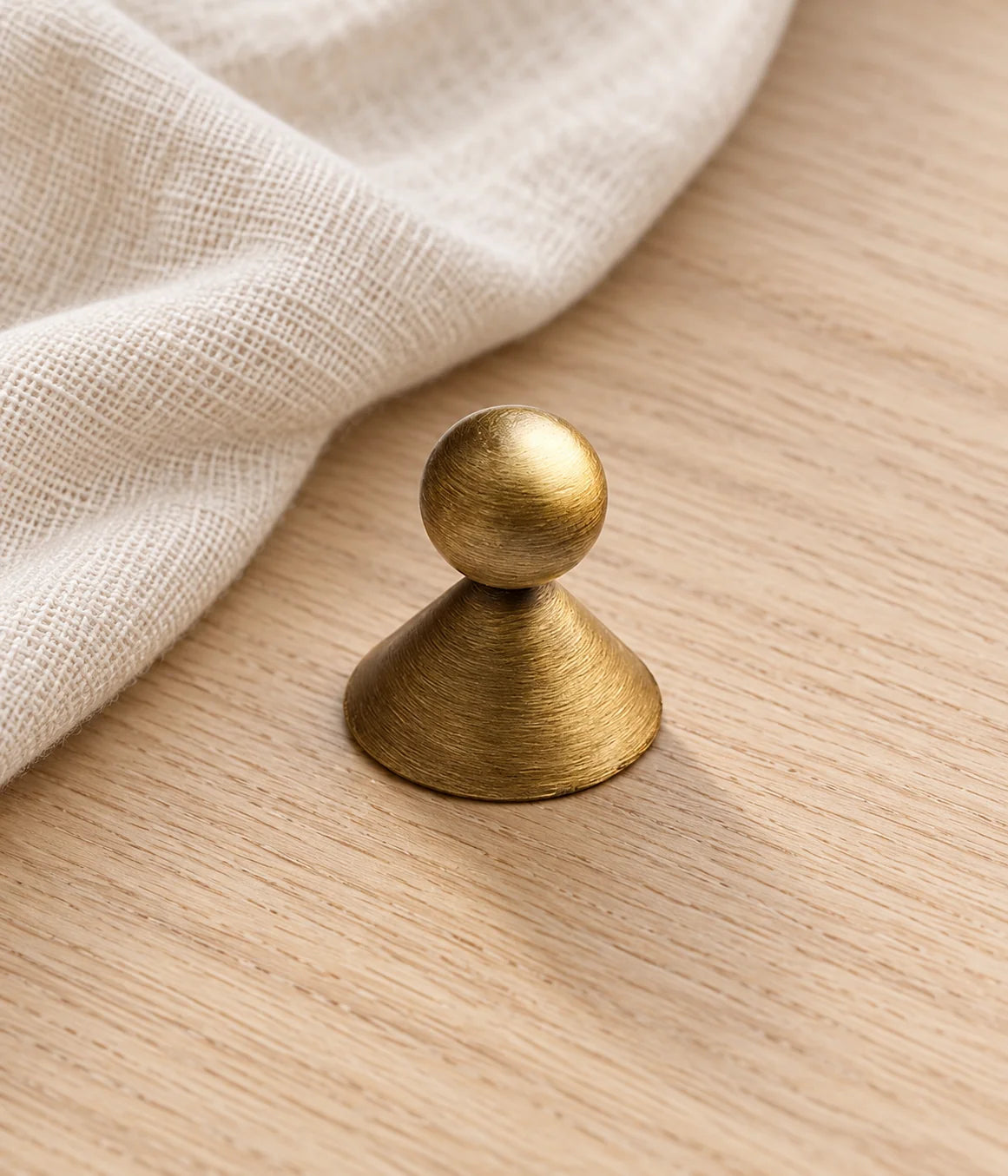 Antique brass ball cabinet knob on pale oak beside cream linen