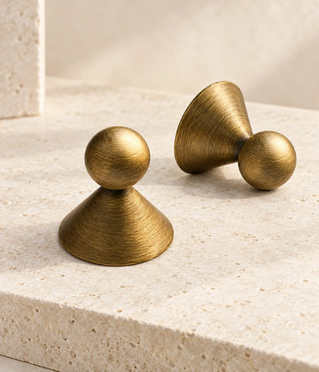Antique brass ball cabinet knobs with wide conical bases arranged on ivory stone