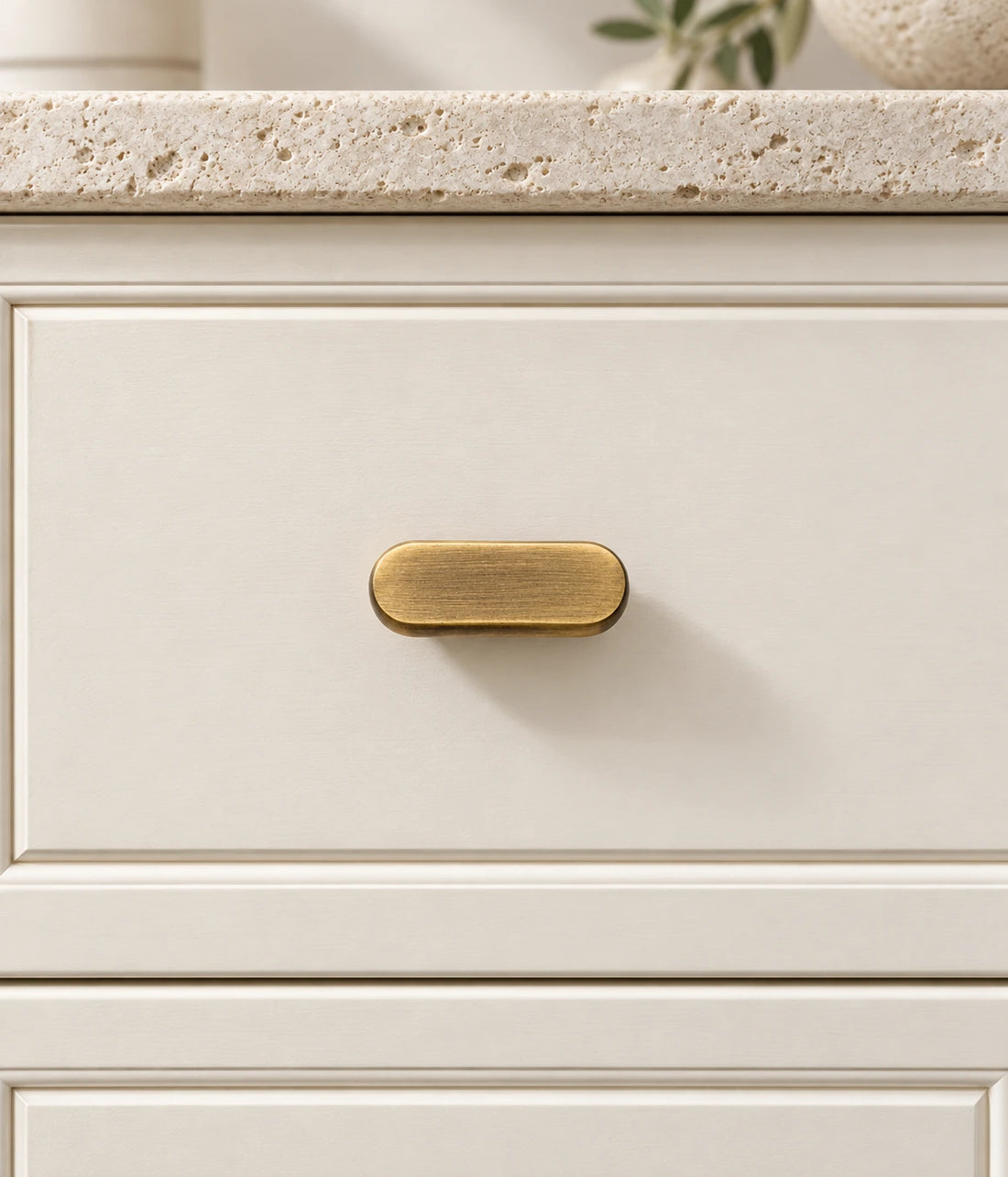 Antique brass cross knob and oval T-knob arranged on pale travertine