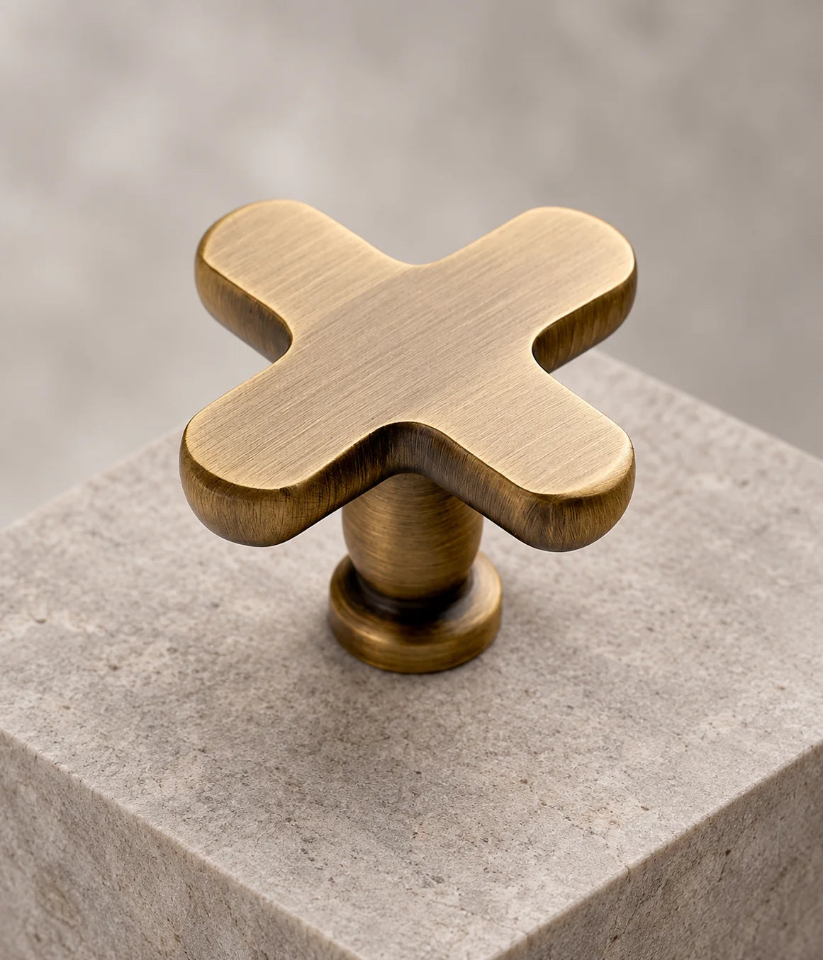 Rounded cross cabinet knob with a flat brushed brass face and round mounting base