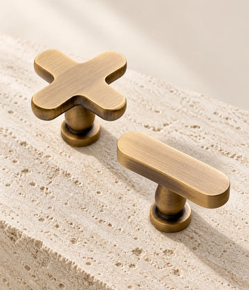 Antique brass cross knob and oval T-knob arranged on pale travertine