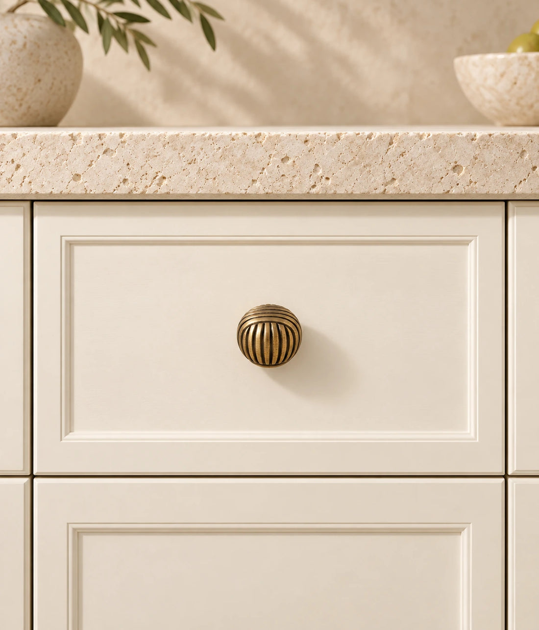 Antique brass cross-ribbed ball cabinet knobs arranged on ivory limestone