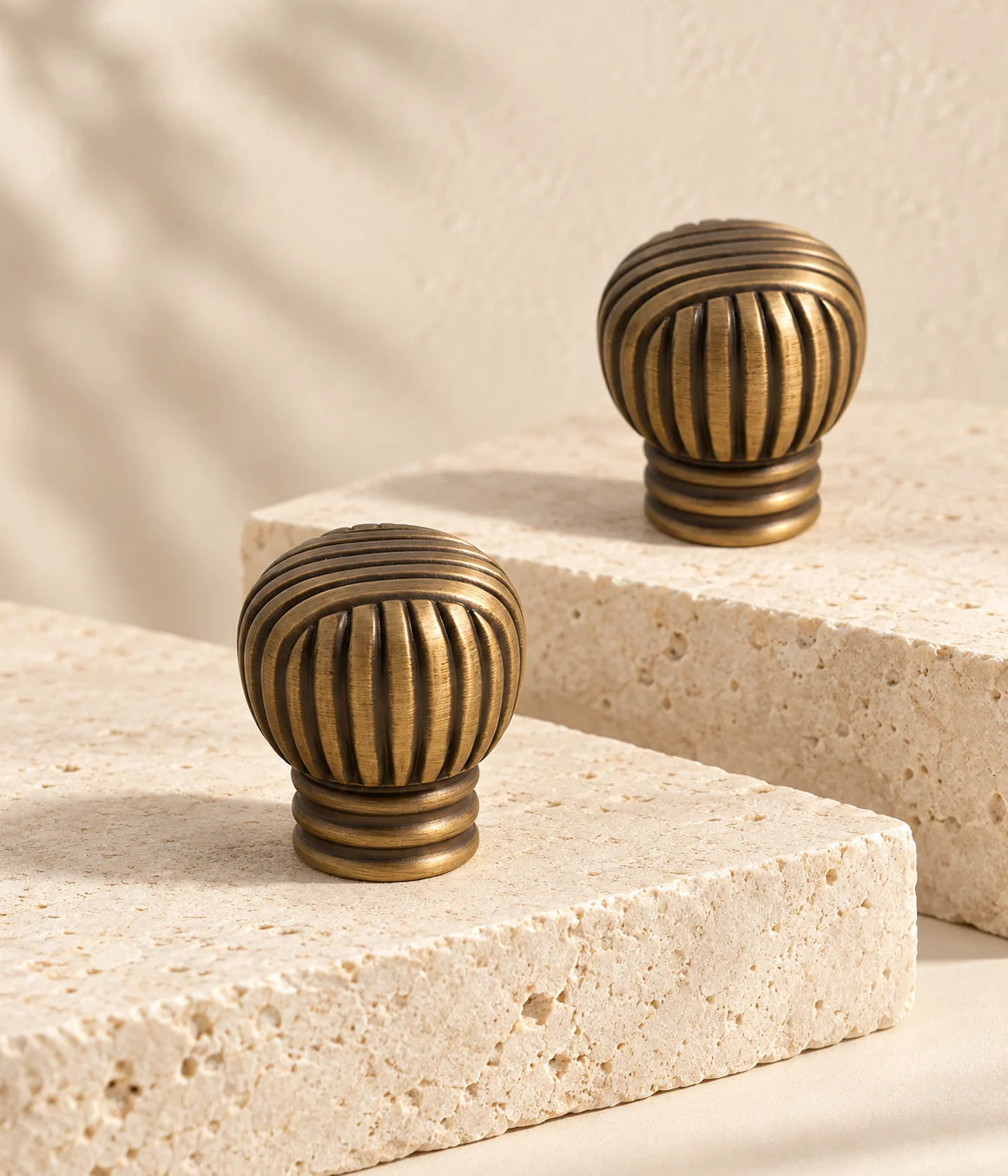 Antique brass cross-ribbed ball cabinet knobs arranged on ivory limestone