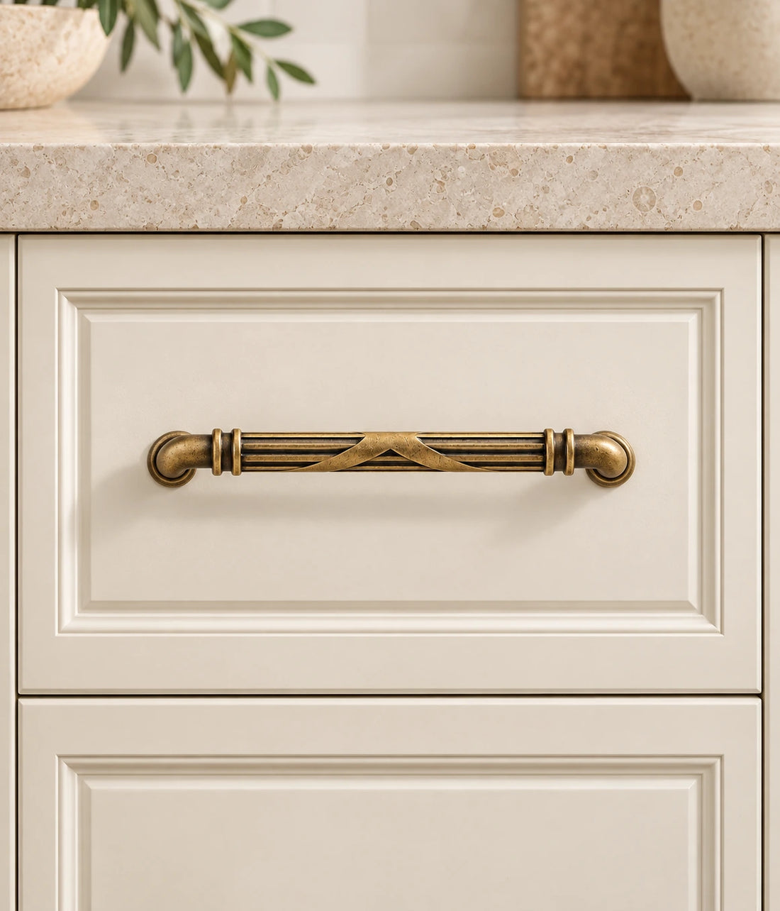 Antique brass cross-ribbon cabinet pulls in three sizes on ivory limestone
