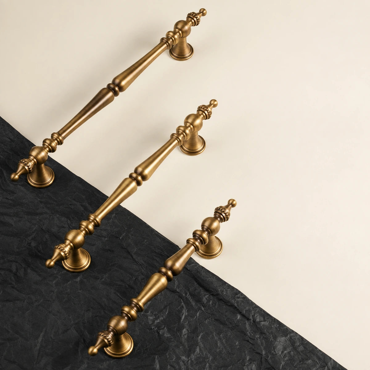 Three antique brass crown finial pulls arranged on cream and black surfaces