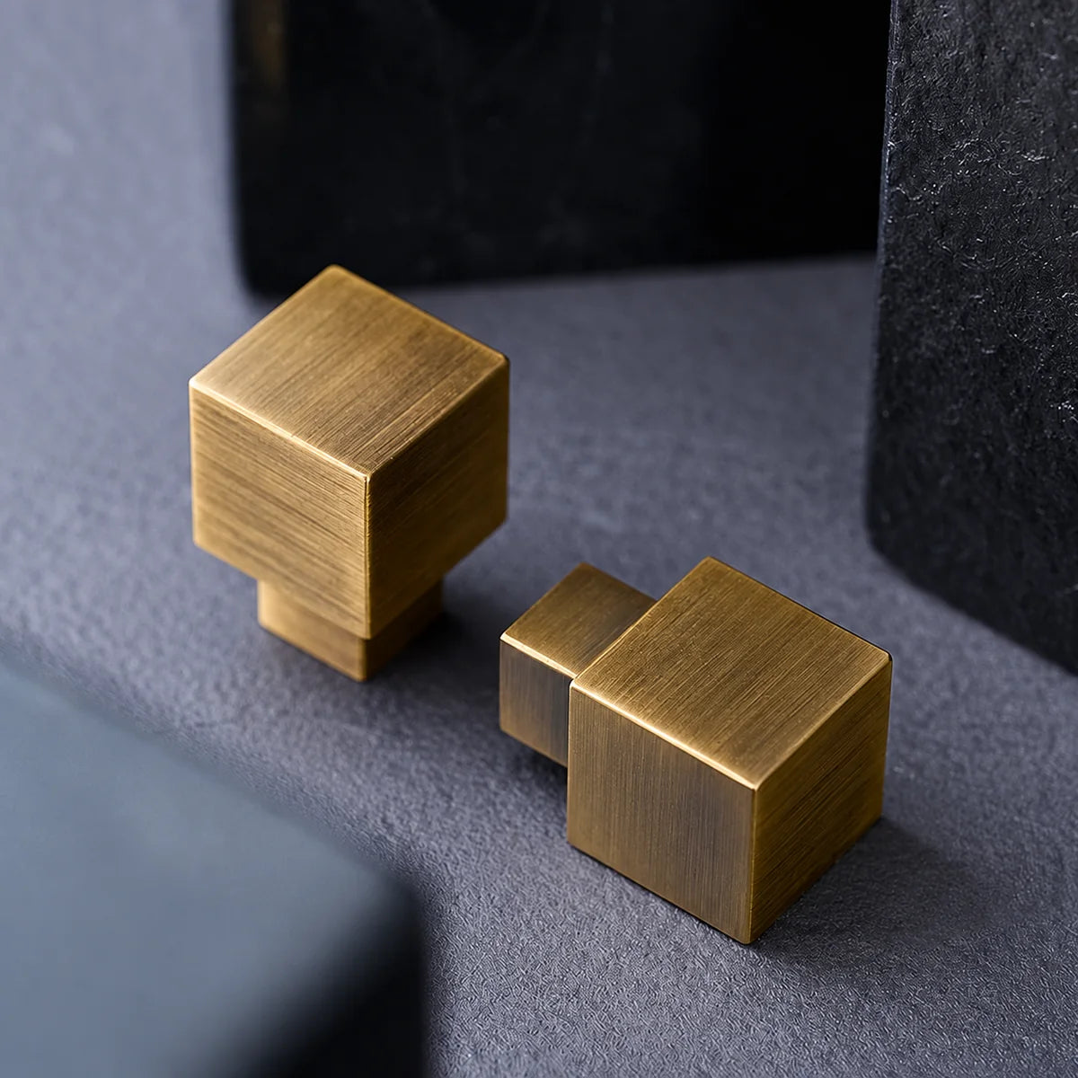 Two antique brushed brass cube knobs showing their square faces and stems