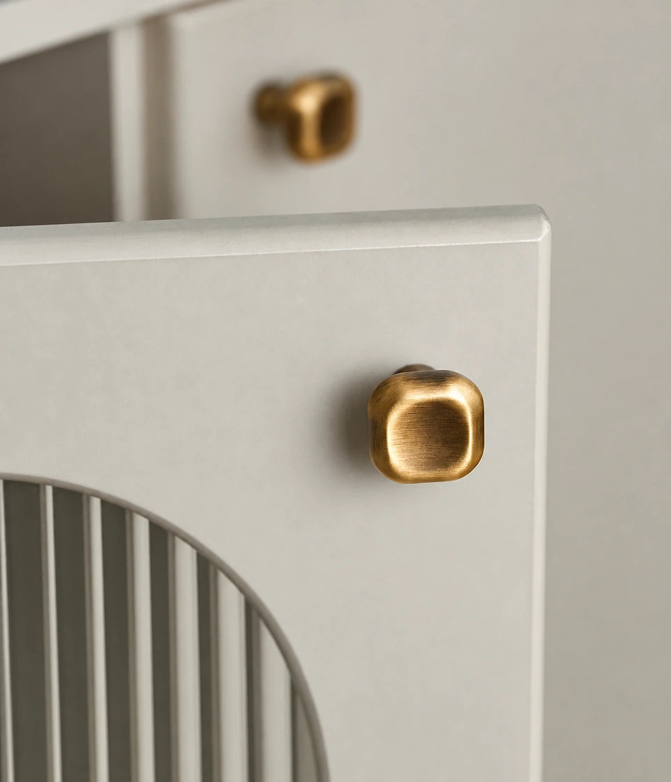 Rounded-square antique brass cushion knob on a curved cabinet door