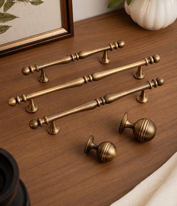 Antique brass decorative cabinet pulls and grooved ball knobs on a wood surface