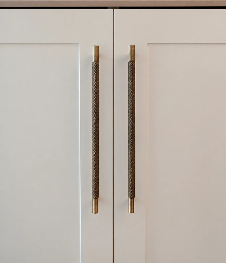 Antique brass diamond-knurled cabinet pulls installed vertically on cream cabinet doors