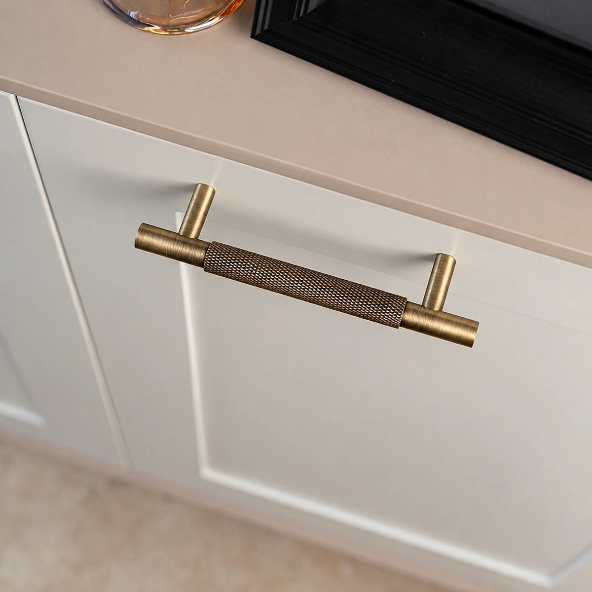 Short antique brass diamond-knurled pull installed horizontally on cream cabinetry