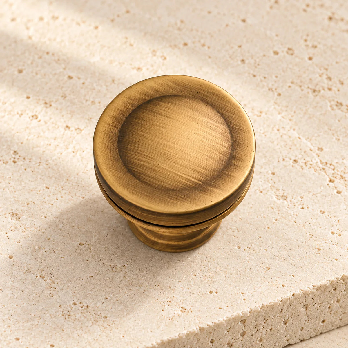antique brass dished cabinet knob on pale limestone.