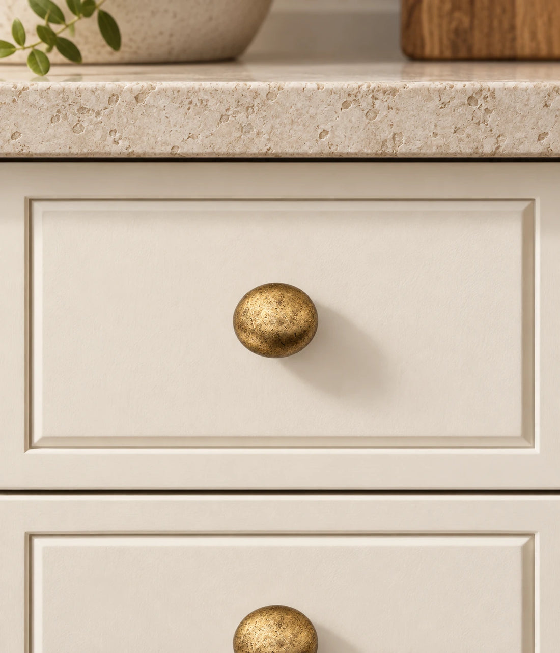 Three distressed antique brass round cabinet knobs arranged on ivory limestone