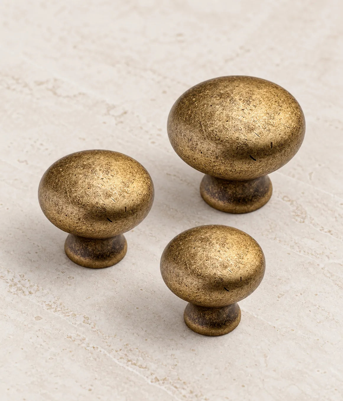 Three distressed antique brass round cabinet knobs arranged on ivory limestone